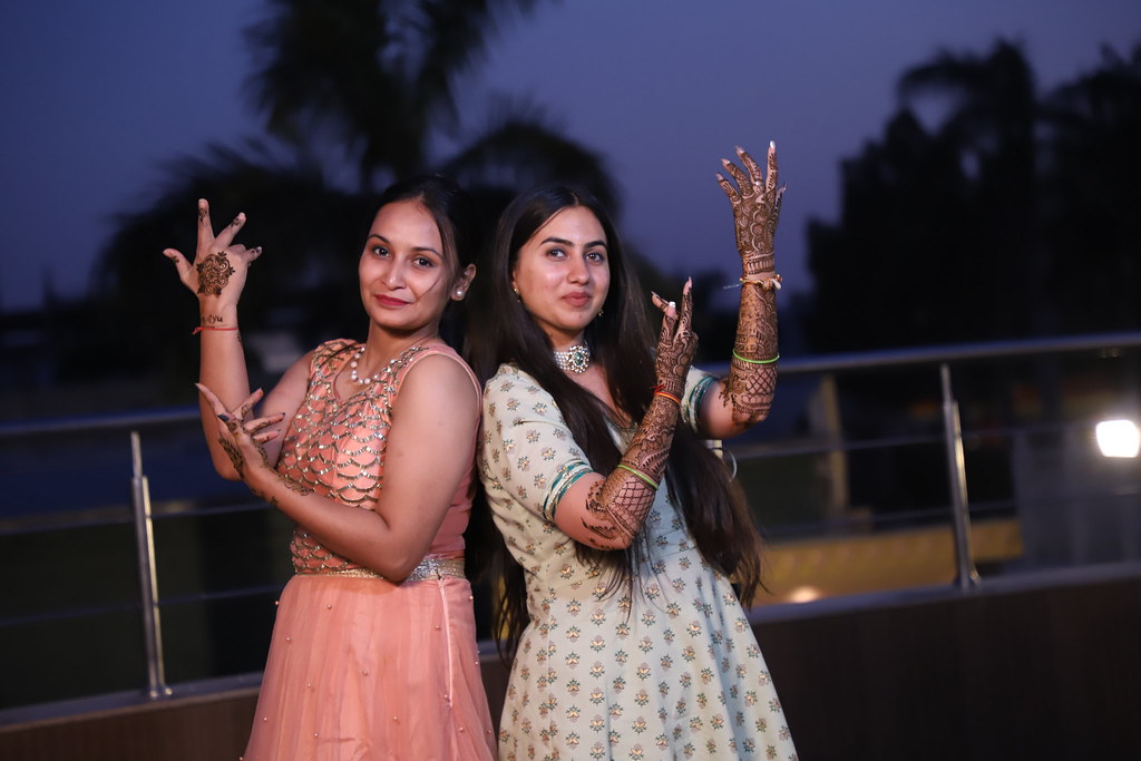 Two women showing henna-decorated hands and arms at an evening mehndi ceremony
