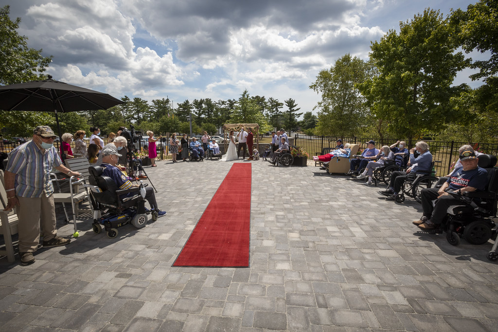 A wide shot of the same veterans' home wedding ceremony, showing the full courtyard and dozens of onlookers