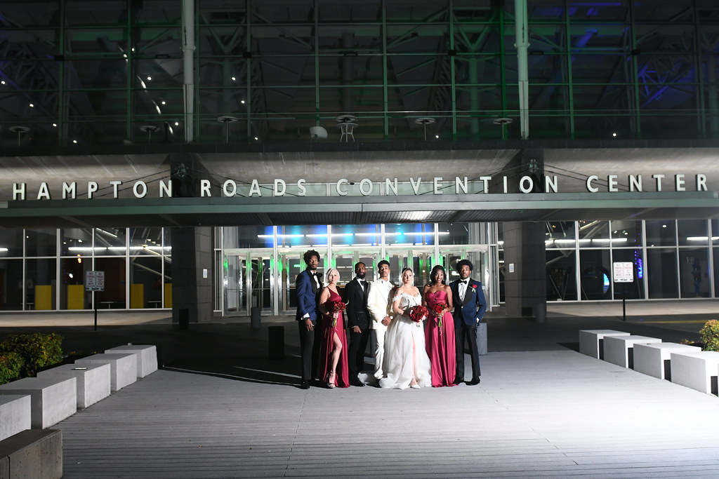 A wedding party of seven people posing together at night outside a convention center